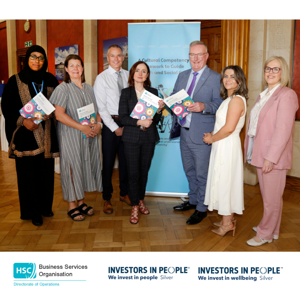 Health Minister Mike Nesbitt standing with the report and the speakers of the event. A mix of males and females standing in front of a pull up stand