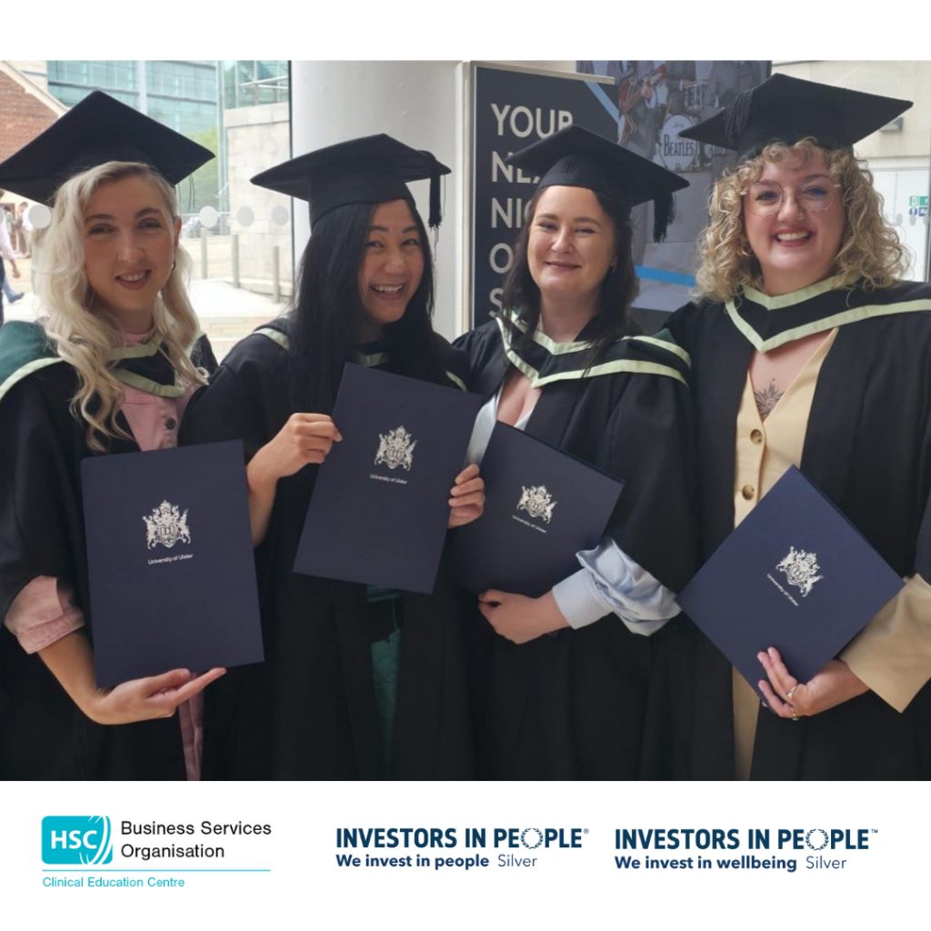 Four women standing in graduation robes with certificates from the University of Ulster