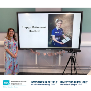 Heather Finlay standing beside a retirement presentation displaying a congratulatory message and photograph from her nursing career.