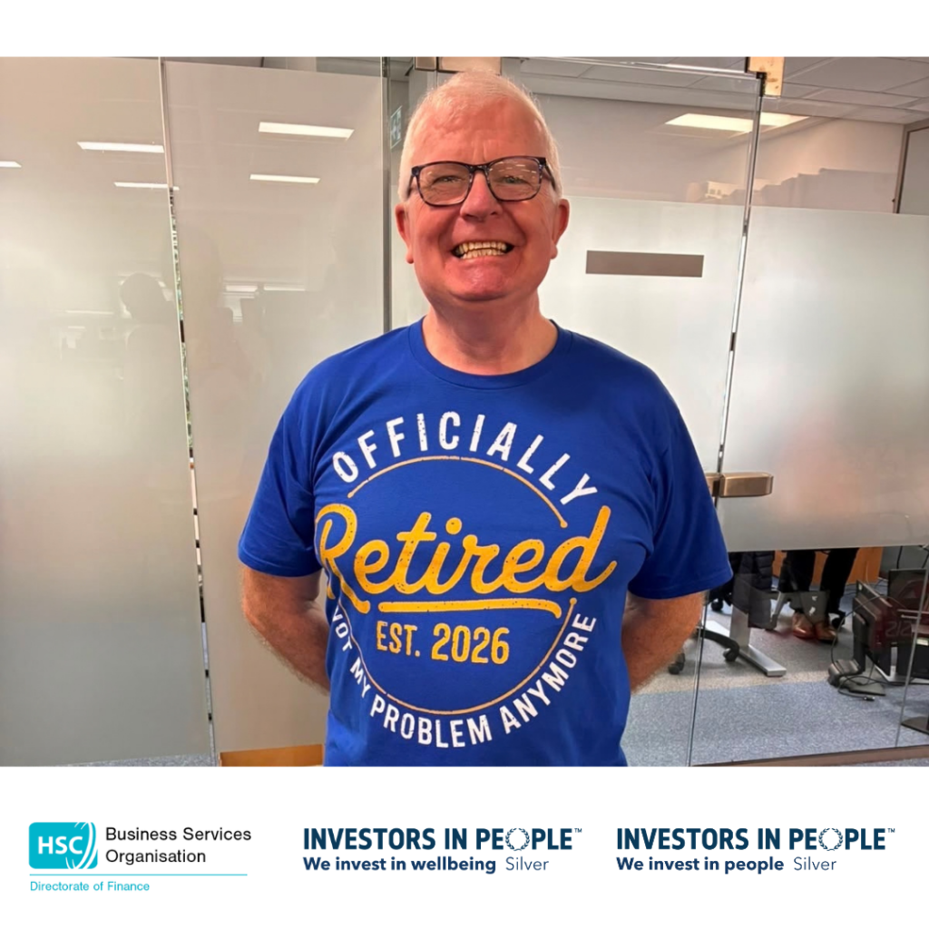 A person stands in an office meeting room in front of glass partition walls. The person is wearing a blue T-shirt with the text: “Officially Retired, Est. 2026, Not My Problem Anymore.” The image appears to mark a retirement celebration. At the bottom of the graphic are the logos for the Health and Social Care Business Services Organisation (BSO) Directorate of Finance and Investors in People Silver accreditation. Visible text on T-shirt: “Officially Retired Est. 2026 Not My Problem Anymore” 