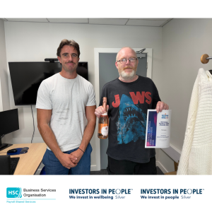 Two colleagues standing in an office, with one colleague holding a National Payroll Week 2026 Payroll Dedication Award certificate and a bottle of sparkling wine. The photo is branded with Business Services Organisation Payroll Shared Services and Investors in People Silver logos along the bottom.
