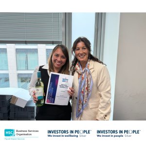 Two colleagues standing beside a window in an office, with one colleague holding a National Payroll Week 2026 Payroll Dedication Award certificate and a bottle of wine. The image includes Business Services Organisation Payroll Shared Services and Investors in People Silver branding along the bottom.