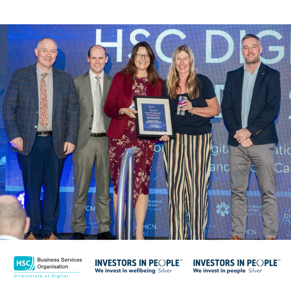 Group photograph on an awards stage showing two award recipients holding a framed winner certificate, accompanied by three presenters. HSC Digital Awards branding is displayed in the background, with HSC Business Services Organisation and Investors in People Silver logos below.